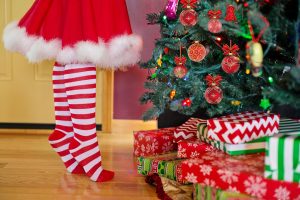 Girl wearing red dress and white and red striped socks decorating a Christmas tree with presents underneath it