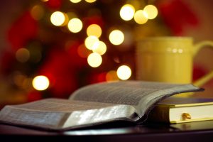 Bible open near cup and Christmas tree