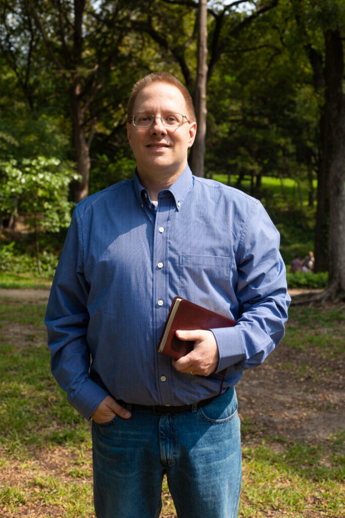 John Rothra outdoors wearing a blue shirt and jeans holding a Bible